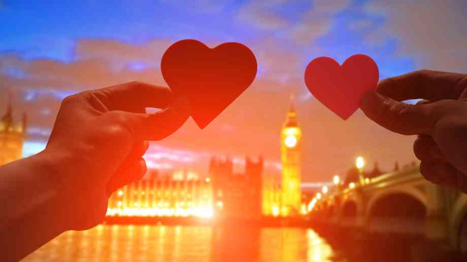 Two people hold up hearts with Houses of Parliament in the background.