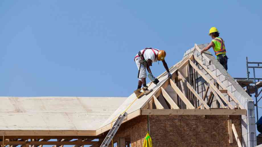Two construction workers work on the roof of a partially-built house.