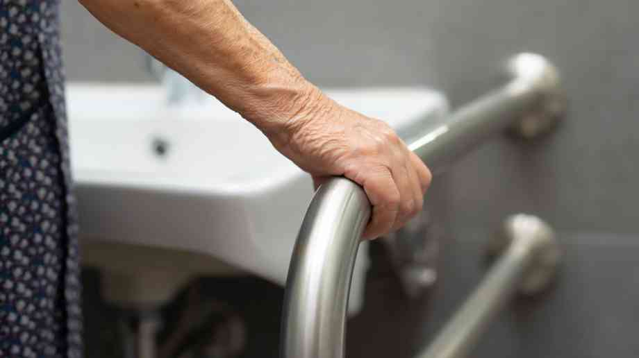 Elderly woman using handrail in bathroom.